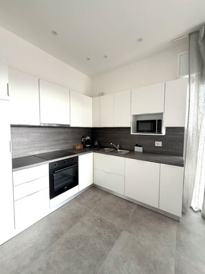 A modern kitchen with white cabinets, a built-in microwave, a stove, and a sink. - Velù Apartment - Ludovica (Veneto)