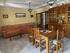 Un comedor con mesa de madera, sillas, sofá y un aparador con objetos decorativos.