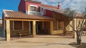 A two-story building with a red facade, a tiled roof, and a covered patio area with benches. - Rural House 'Casa Bartolo' with Mountain Views, Wi-Fi and Air Conditioning (Vélez-Rubio)