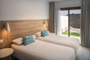 A hotel room with two beds, a round side table, a wall-mounted lamp, and a view of a courtyard through a glass door. - Ereza Villas La Granja (Yaiza)
