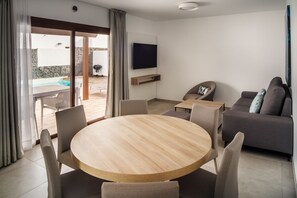 A modern living room with a round wooden table, grey sofa, and a flat-screen TV mounted on the wall. - Ereza Villas La Granja (Yaiza)