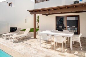 A patio with a white table and chairs, a pool, and a covered area with a grill. - Ereza Villas La Granja (Yaiza)