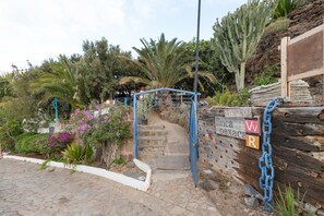 Un sentiero in pietra conduce a un cancello con una targa, circondato da cactus e piante fiorite.