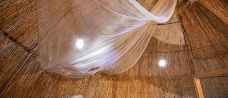 Una habitación con una cama, mosquitero colgante y techo tejido.
