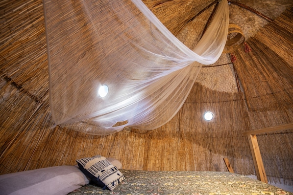 A room with a bed, a hanging mosquito net, and a woven ceiling.