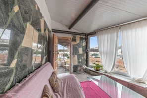 Une chambre avec un lit, une fenêtre avec des rideaux, un ventilateur et une vue sur l’extérieur.