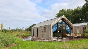 Ein modernes Haus mit geneigtem Dach, einer Terrasse mit Sitzgelegenheiten und einem Garten.