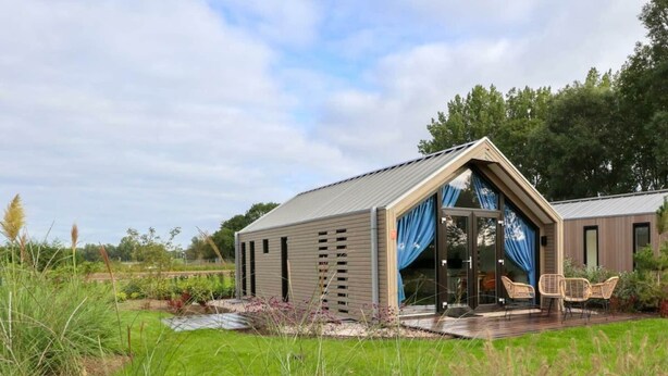 Ein modernes Haus mit Satteldach, einer Terrasse mit Stühlen und einem Garten.