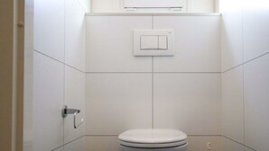 Ein Badezimmer mit Toilette, Mülleimer, Handtrockner und Lichtschalter an der Wand.