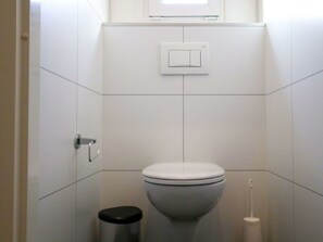 A bathroom with a toilet, a trash bin, a hand dryer, and a light switch on the wall. - Holiday Home in Nijkerk With Terrace (Nijkerk)