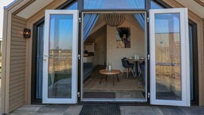Ein modernes, eingeschossiges Gebäude mit großem Glastür-Eingang, einem Essbereich mit Tisch und Stühlen sowie einer durch die Glasfront sichtbaren Küche.