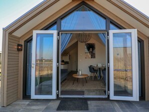 A modern, single-story building with a large glass door entrance, a dining area with a table and chairs, and a kitchen visible through the glass. - Holiday Home in Nijkerk With Terrace (Nijkerk)