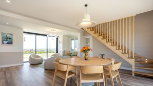 A modern dining area with a wooden table and chairs, a vase of flowers, and a staircase with wooden railings.