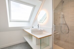 Uma casa de banho moderna com clarabóia, lavatório redondo e cabine de duche com divisória de vidro.