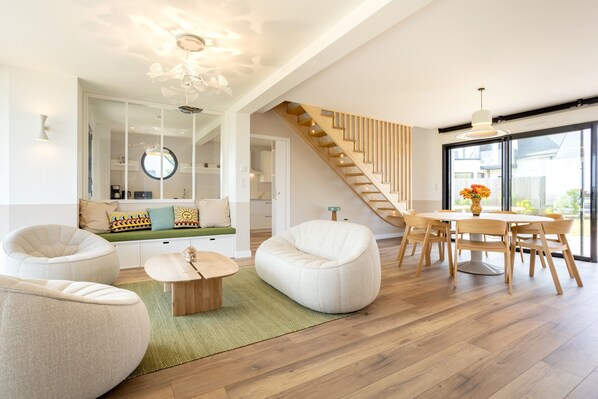 Un salon moderne avec un escalier, un coin repas et une vue dégagée grâce à de grandes fenêtres.