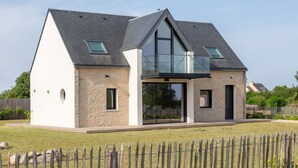 A modern house with a stone facade, a large glass balcony, and a sloped roof.