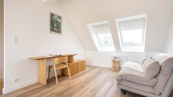 A room with a wooden desk, a cushioned sofa, and a painting on the wall.