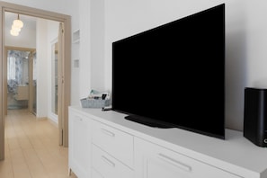 A modern living room with a large flat-screen TV mounted on a white cabinet, a remote control, and a speaker on the right. - Holiday Home 'Apartment For 6 People Near The Sea' with Balcony, Wi-Fi and Air Conditioning (Alghero)
