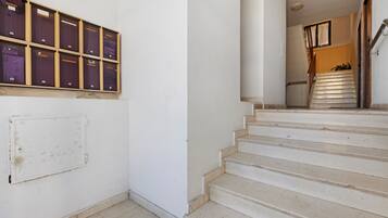Eine Treppe mit weißen Stufen führt zu einer Zwischenebene, an einer Wand stehen Aufbewahrungsboxen und am oberen Ende der Treppe befindet sich eine Tür.