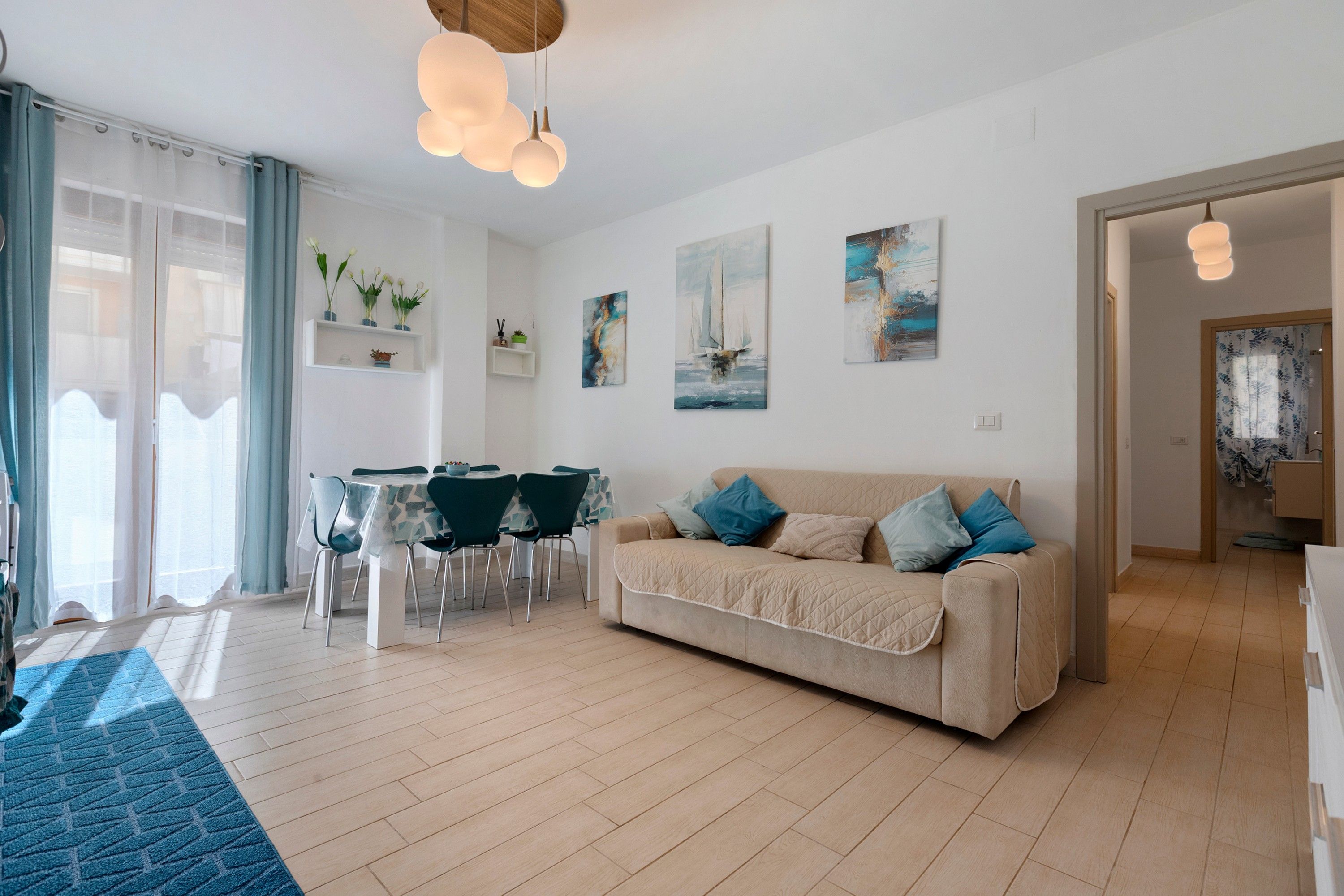 Un salon moderne avec un canapé beige, une table à manger avec des chaises et des œuvres d’art accrochées aux murs.