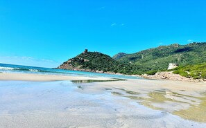 Una spiaggia con acque cristalline, una costa sabbiosa e colline verdi sullo sfondo.