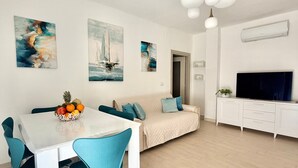 A modern living room with a dining area, a sofa, a TV, and artwork on the walls. - Holiday Home 'Apartment For 6 People Near The Sea' with Balcony, Wi-Fi and Air Conditioning (Alghero)