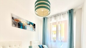 A hotel room with two beds, a tufted headboard, a painting on the wall, and a window with curtains. - Holiday Home 'Apartment For 6 People Near The Sea' with Balcony, Wi-Fi and Air Conditioning (Alghero)
