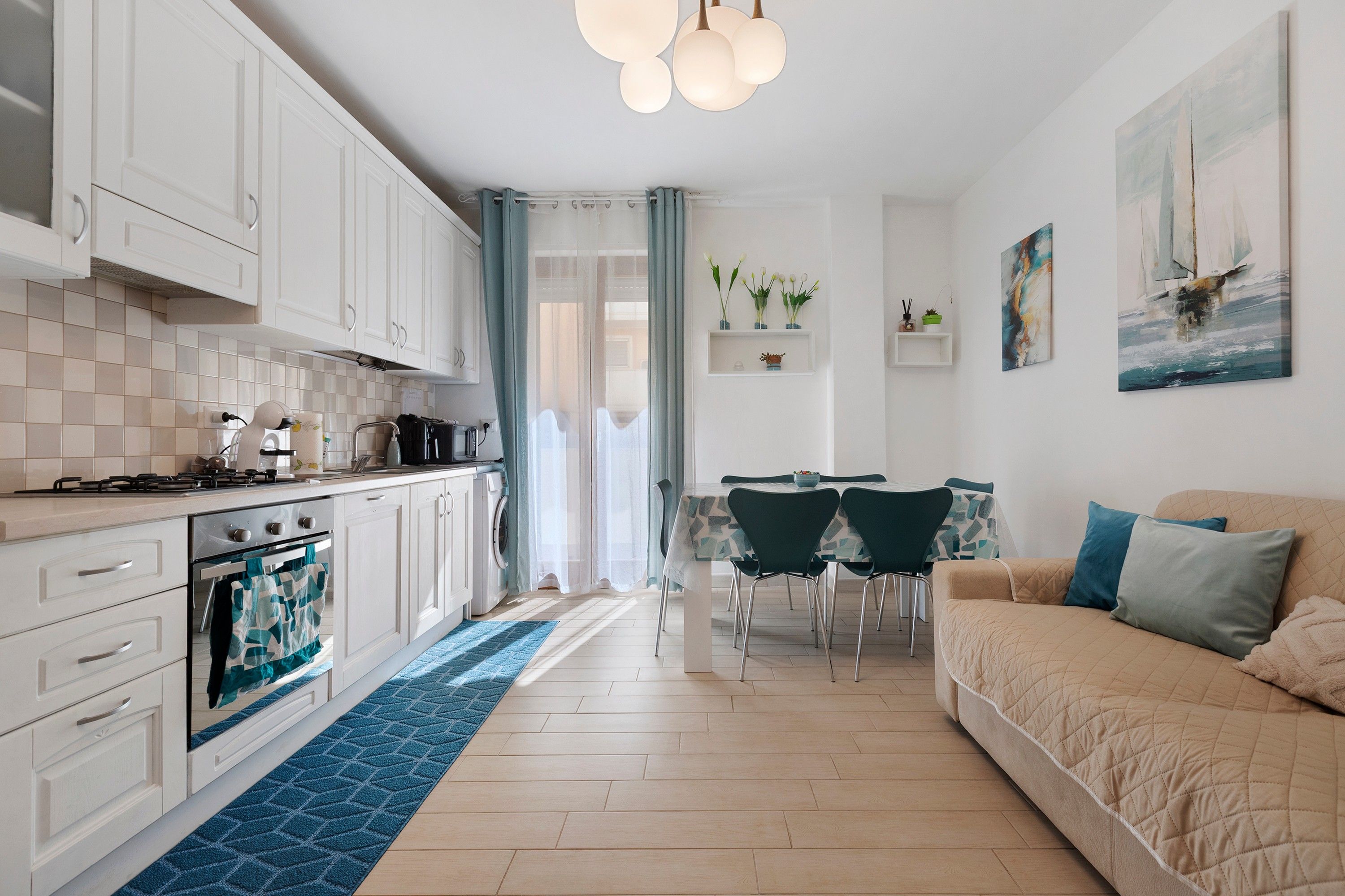 Een moderne keuken met witte kasten, een eethoek met een tafel en stoelen, en een woonkamer met een bank.