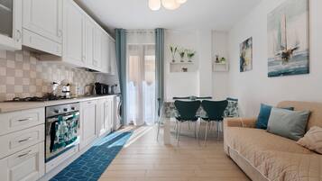Een moderne keuken met witte kasten, een eethoek met een tafel en stoelen, en een woonkamer met een bank.