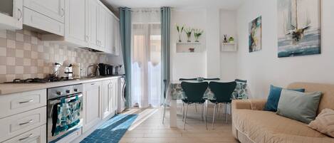 A modern kitchen with white cabinets, a dining area with a table and chairs, and a living room with a sofa.