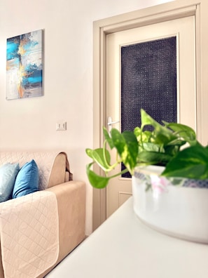 Ein Zimmer mit einem beigefarbenen Sofa, einer Topfpflanze, einer Tür mit satiniertem Glas und einem an der Wand hängenden abstrakten Gemälde.