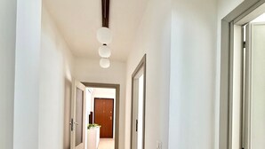 A hallway with a light-colored tiled floor, white walls, and a door at the end leading to a room with a wooden door. - Holiday Home 'Apartment For 6 People Near The Sea' with Balcony, Wi-Fi and Air Conditioning (Alghero)