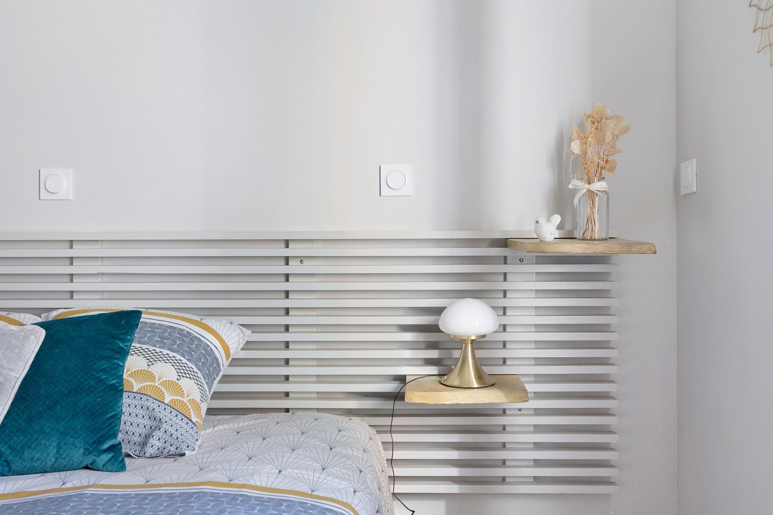 Un dormitorio ordenado con cama, mesita de noche, lámpara y un jarrón decorativo.