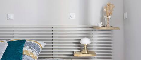 Un dormitorio ordenado con cama, mesita de noche, lámpara y un jarrón decorativo.