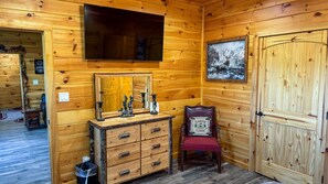 Een houten chalet van binnen, met een televisie, een dressoir, een stoel en een deur.