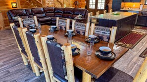 Uma mesa de jantar de madeira com cadeiras, um sofá de couro e uma área de cozinha.