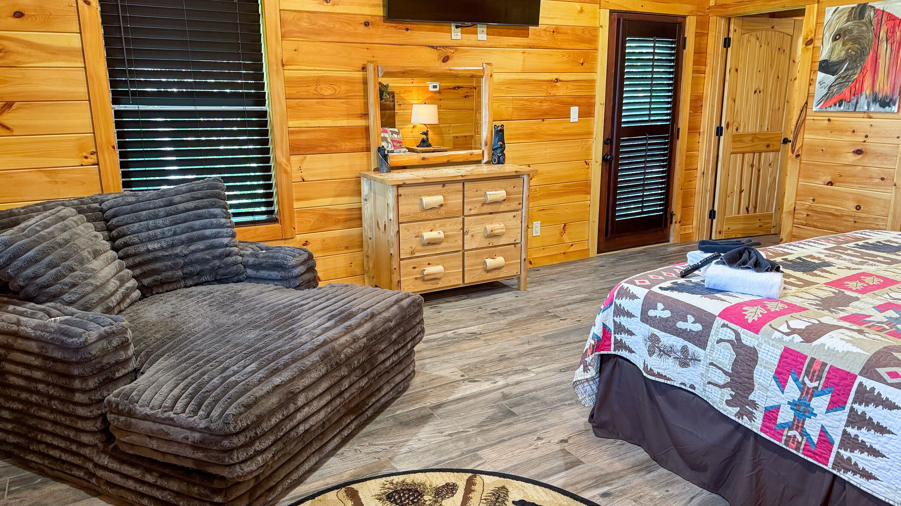 Une pièce aménagée dans le style d’un chalet en rondins, avec un lit, un canapé, une commode en bois et un téléviseur fixé au mur.