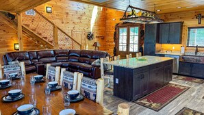Ein Interieur einer Blockhütte mit einem ledernen Ecksofa, einer Kücheninsel und einem Essbereich mit einem Holztisch, gedeckt für vier Personen.