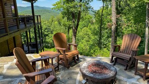 Eine Holzdiele mit Adirondack-Stühlen und einem Steinkamin, mit Blick auf einen bewaldeten Berg.