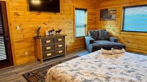 Quarto de cabana de tronco com cama, cômoda e duas janelas.