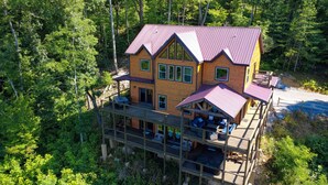 Eine mehrstöckige Holzhütte mit rotem Dach, umgeben von dichtem Wald.