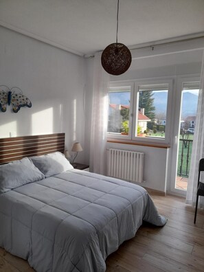 Un dormitorio con cama, ventana, radiador y vistas a casas y montañas.