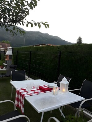Un patio con una mesa lista para comer, sillas exteriores, un farol blanco y vistas a montañas.