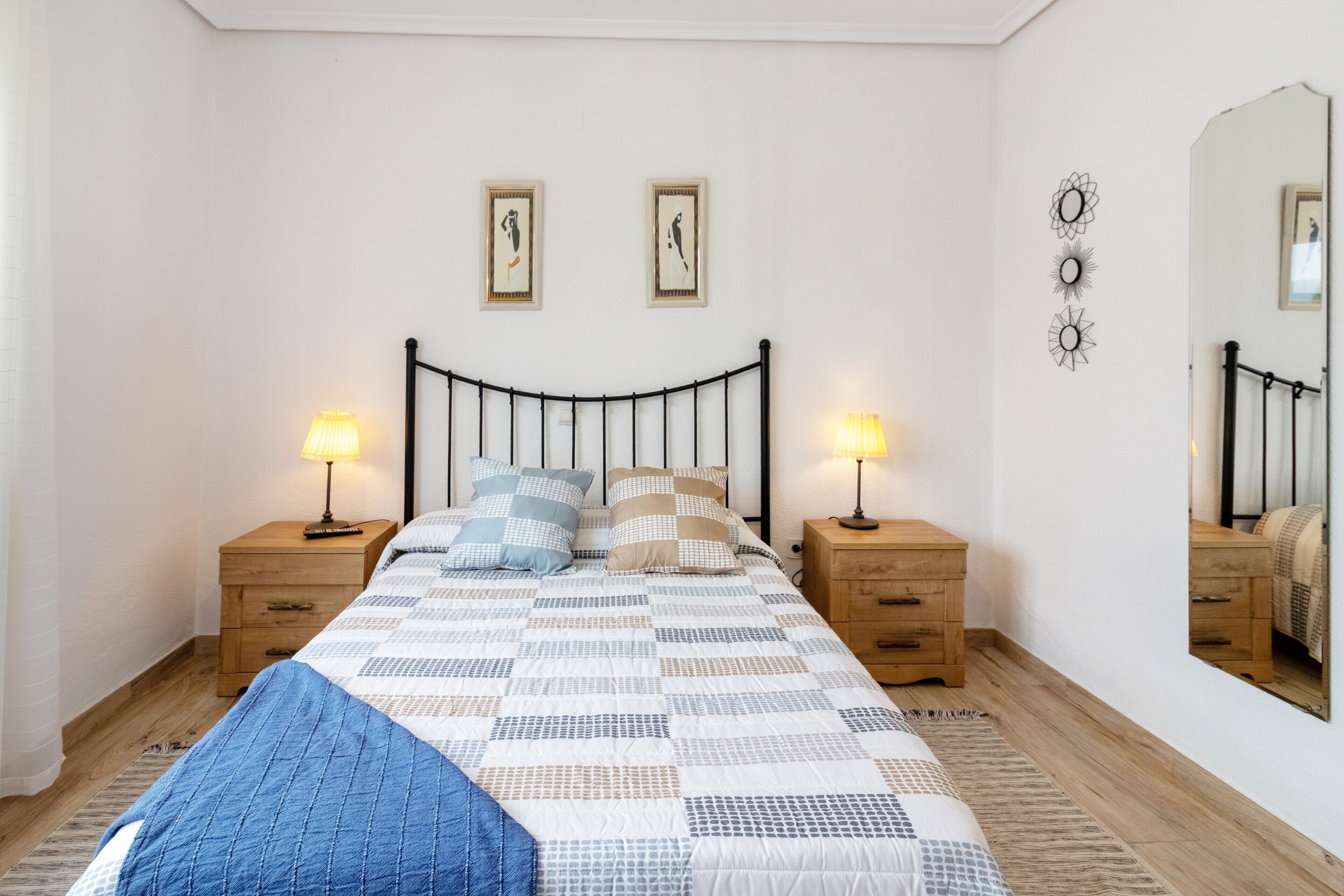Ein Schlafzimmer mit einem Bett, zwei Nachttischen, einem Spiegel und Wandbildern.