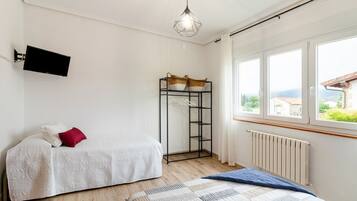 A bedroom with a bed, a small table with a basket, a radiator, and a window with a view.