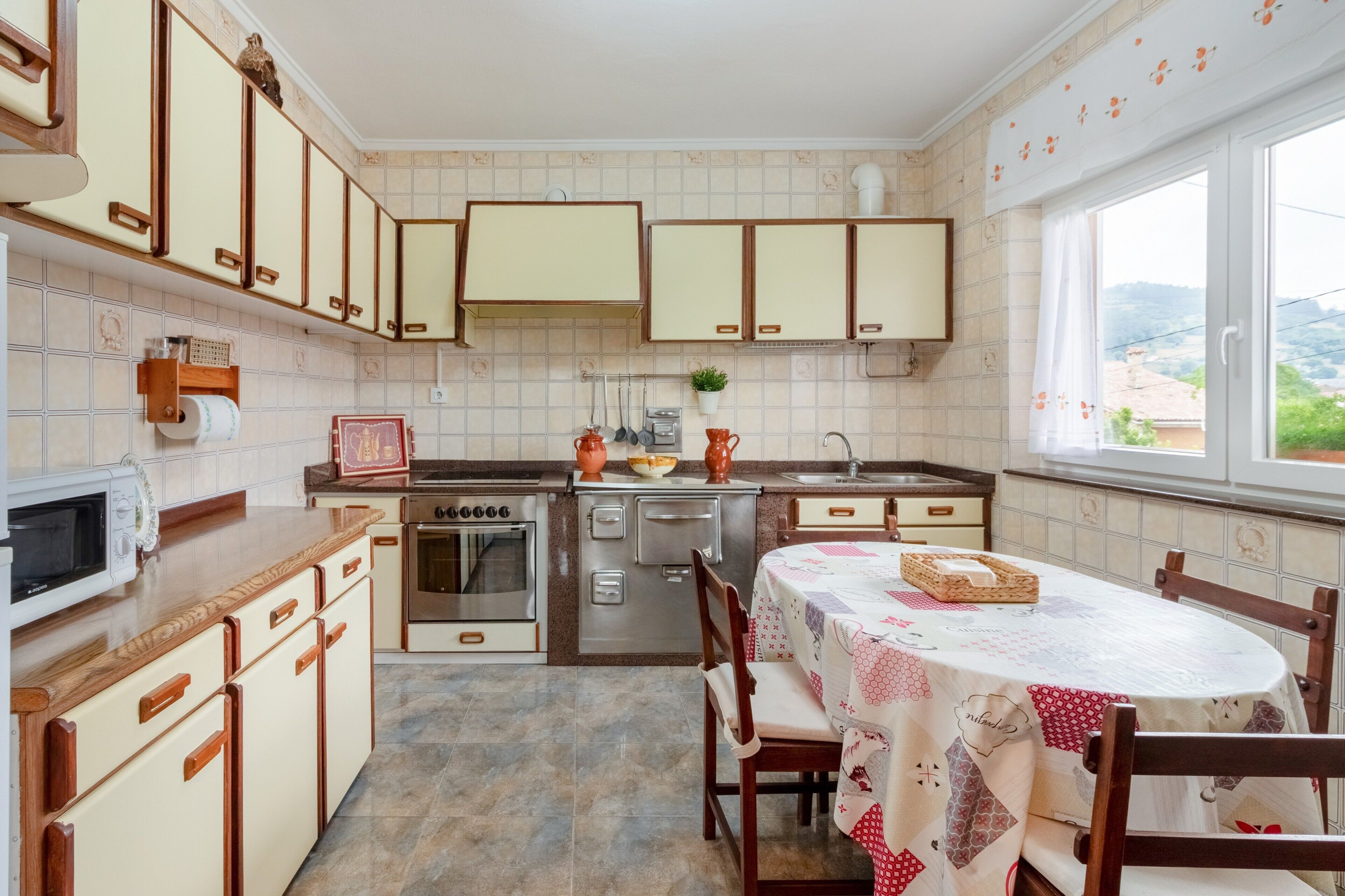 Une cuisine avec des meubles de rangement en bois, une cuisinière, un four à micro-ondes et une table à manger avec des chaises.