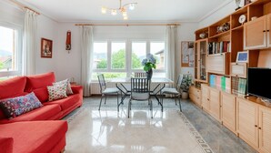 A living room with a red sofa, a dining table with chairs, a TV, and a bookshelf.