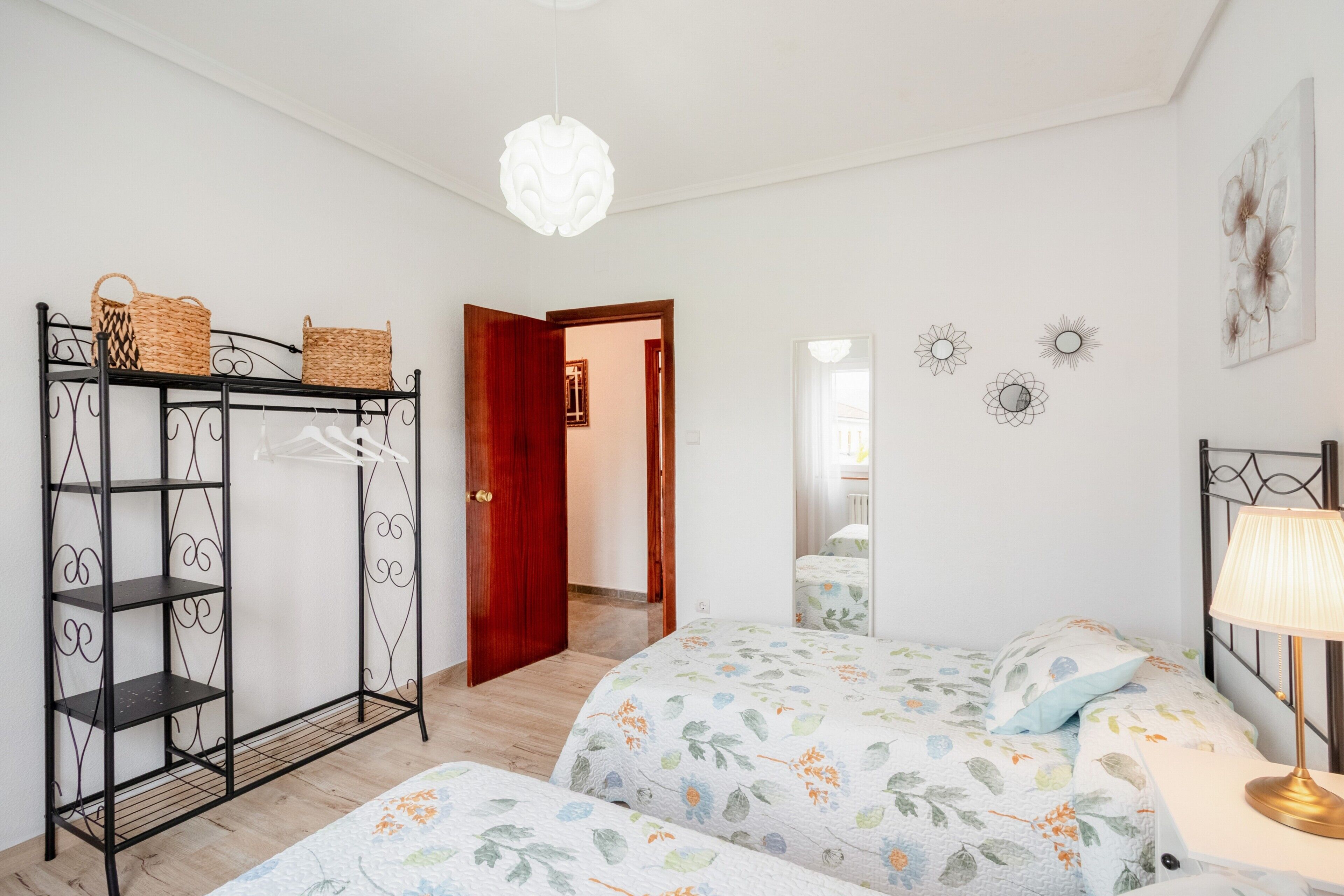 A bedroom with two beds, a wardrobe, a hanging light fixture, and a door leading to another room.