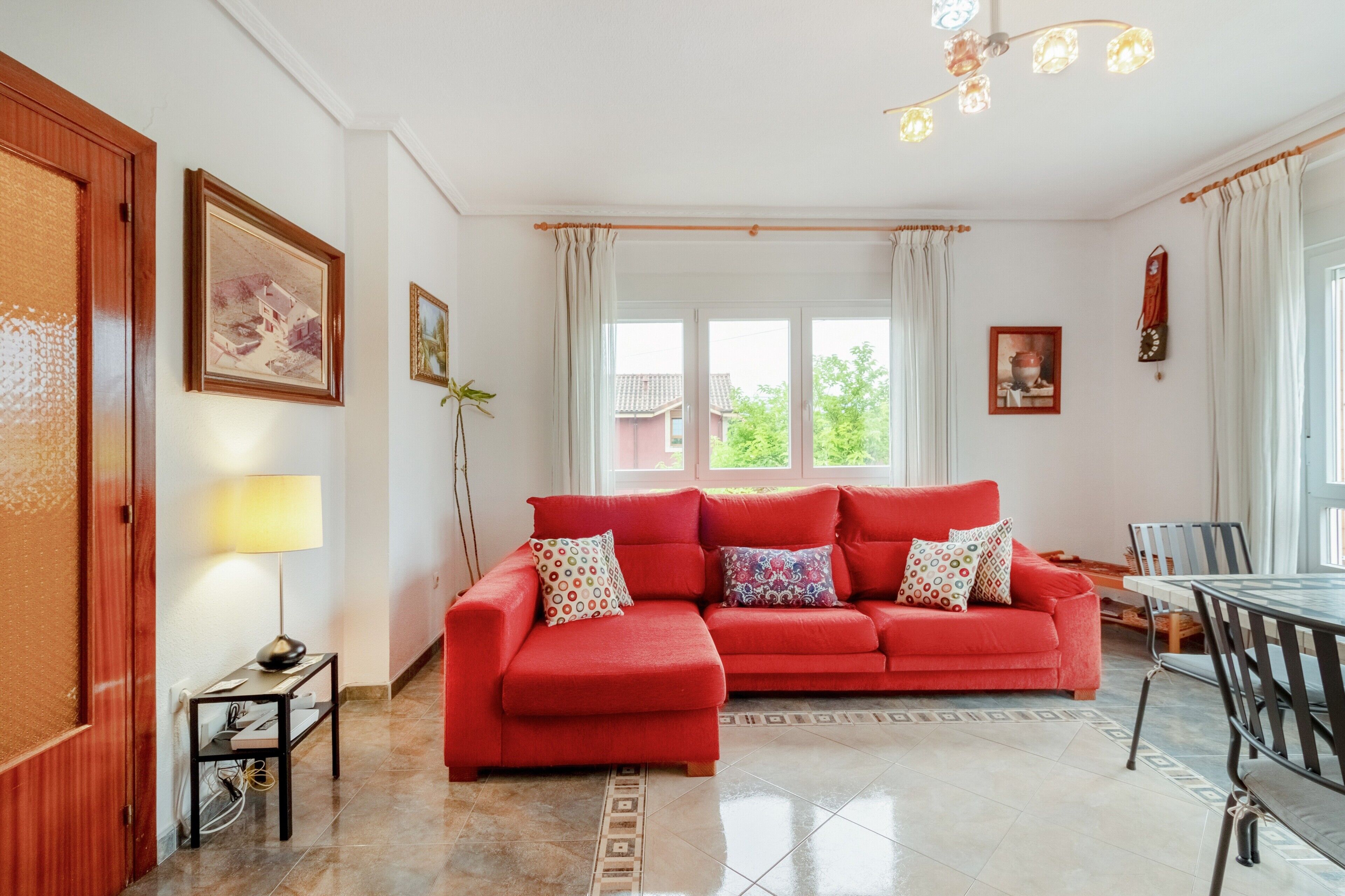 A living room with a red sofa, a dining table, and a chandelier.