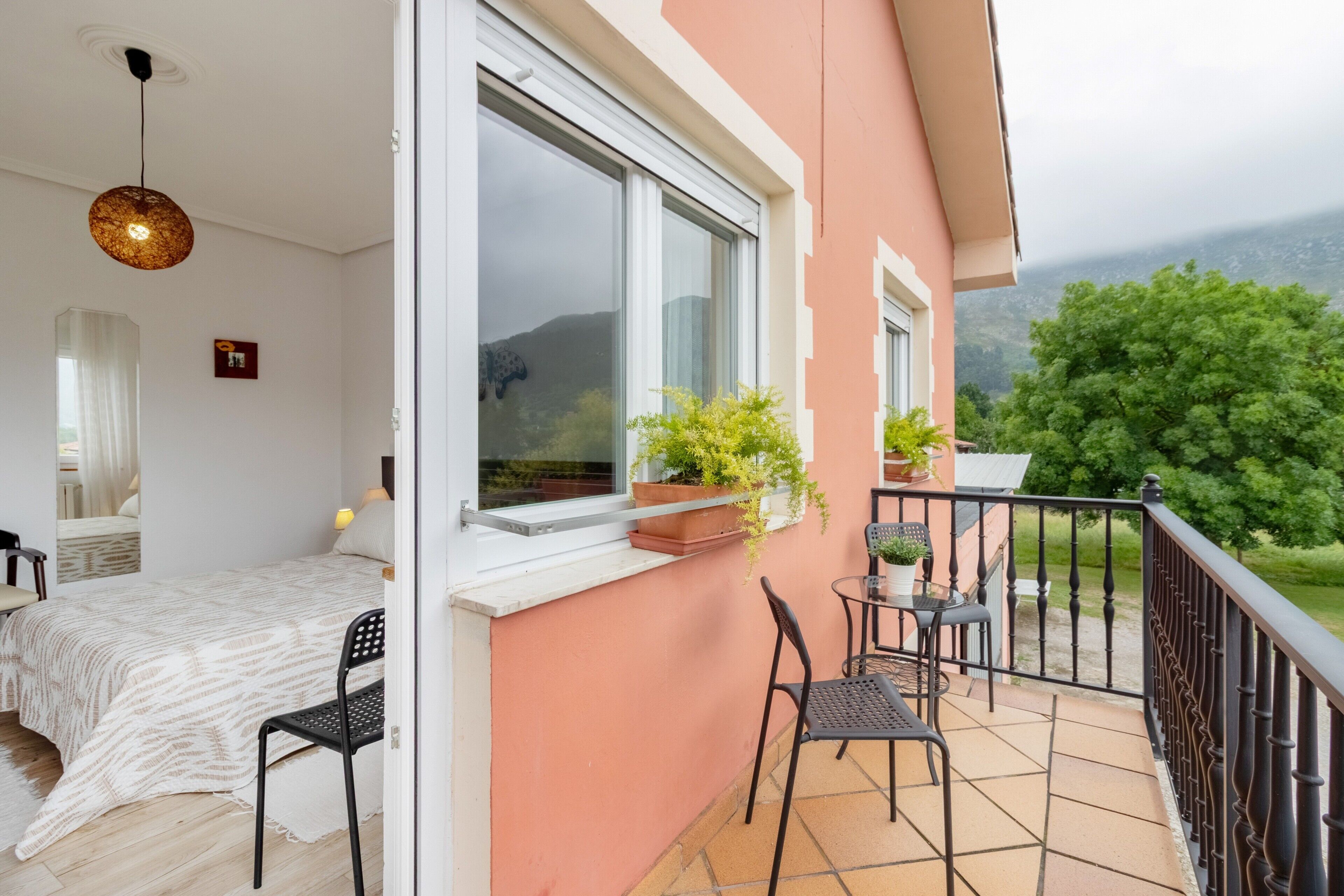 Ein Balkon mit Tisch und Stühlen, ein Bett mit weißer Bettdecke und Blumentöpfe am Fensterbrett.